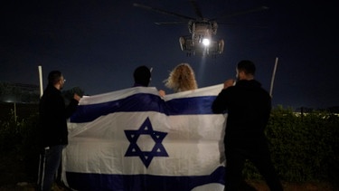 28.11.2023, Israel, Tel Aviv: Menschen, die eine israelische Flagge halten, beobachten die Ankunft eines Hubschraubers, der israelische Geiseln, die von der Hamas freigelassen wurden, zum Ichilov-Krankenhaus in Tel Aviv bringt. Die Hamas und Israel haben im Rahmen einer brüchigen Waffenruhe, die am Dienstag einen fünften Tag hielt, weitere Geiseln und Gefangene freigelassen. | Bild: dpa-Bildfunk/Leo Correa