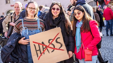 Drei Frauen halten ein Schild in der Hand. Das Wort "Hass" ist mit rot durchgestrichen.  | Bild: picture-alliance/dpa