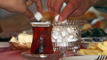 Hände zuckern einen türkischen Tee | Bild: picture-alliance/dpa