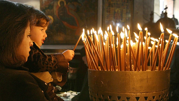 Mutter mit Kind zündet Kerzen in der Kirche an | Bild: picture-alliance/dpa