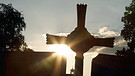 Silhouette eines Kreuzes am Friedhof, hinter dem die Sonne reflektiert | Bild: picture-alliance/dpa