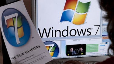 Frau betrachtet das Logo von Windows 7 auf einem Monitor | Bild: picture-alliance/dpa