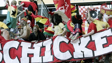 Die Bayern-Anhänger des Münchner Fanclubs "Schickeria München" haben ihre Gesichter schwarz bemalt, tragen Perücken und sind mit ghanaischen Landesfahnen bekleidet (2.4.2005).  | Bild: picture-alliance/dpa
