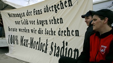 Fans des 1. FC Nürnberg stehen in Nürnberg auf einer Kundgebung vor einem Banner der für den Namen "Max Morlock Stadion" wirbt (1.4.2006). | Bild: picture-alliance/dpa