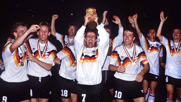 Die deutsche Nationalmannschaft bejubelt den Gewinn der Weltmeisterschaft 1990. Pierre Littbarski reckt den Pokal nach oben. | Bild: imago images
