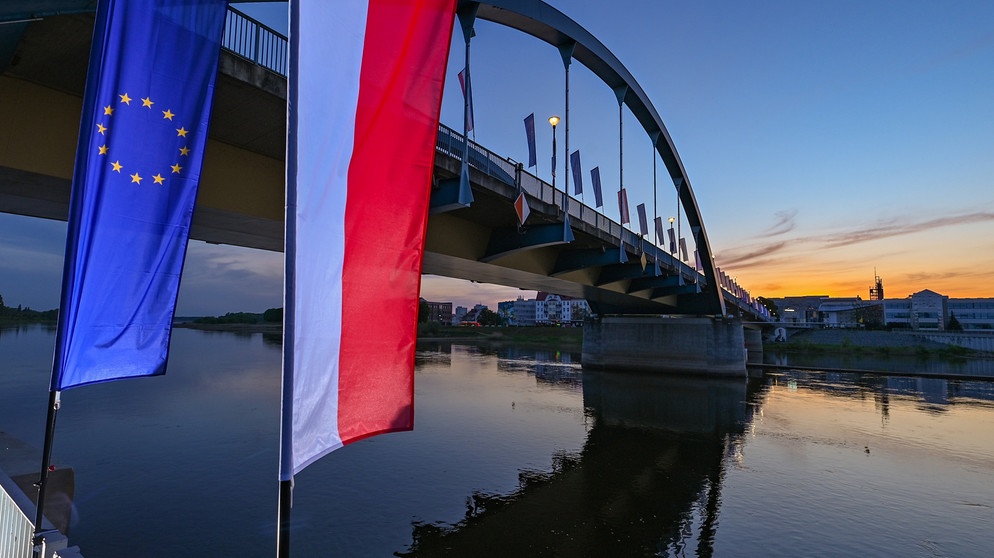 Die Fahne der Europäischen Union und die Nationalflagge Polens wehen im Wind zum Sonnenaufgang vor der Stadtbrücke über den Grenzfluss Oder zwischen Frankfurt (Oder) und dem polnischen Slubice. | Bild: picture-alliance/dpa