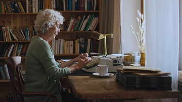 Claretta (Carla Becker) schreibt auf ihrer Schreibmaschine. | Bild: solo:film GmbH/Ute Bolmer