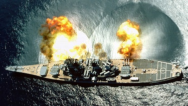 Vogelperspektive auf das Kriegsschiff USS IOWA, das während einer Übung in den Gewässern vor Vieques alle seine 15 Kanonen abfeuert. | Bild: BR/NARA gemeinfrei