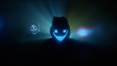Menschen mit leuchteten Masken stehen in dunklen Räumen - Symbol für die dunklen Abgründe des Internets, in denen sich jungen Menschen radikalisieren | Bild: BR