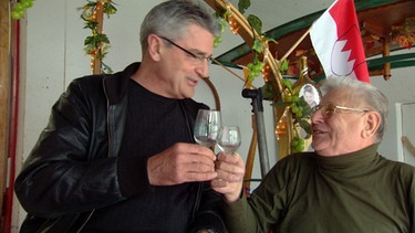 Franz X. Gernstl stößt mit Gustav Weissenseel an. Er ist Konstrukteur der skurrilen Volkacher Weinwagen. | Bild: BR/megaherz gmbh