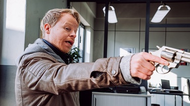 Aufnahmeleiter Sander (Martin Wißner) macht sich einen Spaß daraus, Christian mit der Film-Waffe zu erschrecken. | Bild: BR/Nadya Jakobs