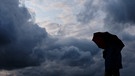 Ein Mann geht mit einem Regenschirm vor aufziehenden dunklen Wolken spazieren.Das Wetter könnte für die Menschen ab Donnerstagnachmittag sehr ungemütlich werden. Der Deutsche Wetterdienst (DWD) erwartet verbreitete Unwetter durch schwere Gewitter und starke Regenfälle im ganzen Land.  Foto: Martin Gerten/dpa +++ dpa-Bildfunk +++ | Bild: dpa-Bildfunk/Martin Gerten
