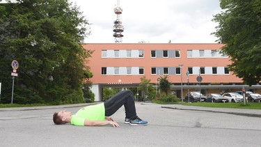 Der Fitnesstrainer Felix Gass ist auf dem Gelände des Bayerischen Rundfunks in Freimann bei den Vorbereitungen mit der Übung Hüftstrecker in Rückenlage zum Lauf 10! zu sehen, Ausgangsposition. | Bild: BR/Felix Hörhager