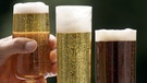 Hand greift nach einem von drei vollen Biergläsern | Bild: picture-alliance/dpa