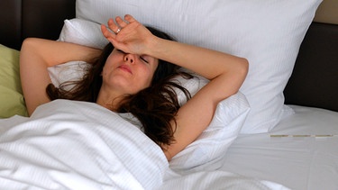 Symbolbild: Frau liegt mit Migräne im Bett | Bild: picture-alliance/dpa