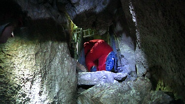 Ein Mann klettert durch einen engen Höhlengang | Bild: BR