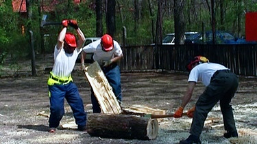 Männer schlagen bei einem Holzfällerwettbewerb mit Äxten auf einen Stamm ein. | Bild: BR