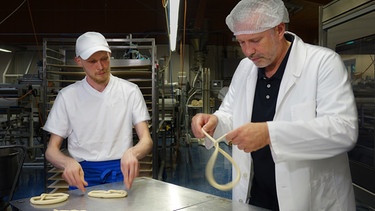 Von links: Franz Piller und Alexander Herrmann an der Brezenteigschlingmaschine in der Produktionsstätte der Bäckerei Piller in Karlsfeld. | Bild: BR / Jürgen Endriß