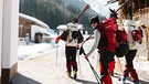 Drei Skifahrer mit Gepäck in einem Dorf zu Fuß unterwegs  | Bild: Moritz Ablinger