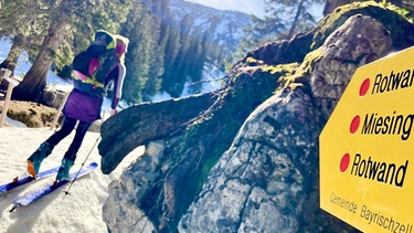 Skitourengeherin passiert einen Wegweiser zu Rotwand und Miesing  | Bild: Michael Vitzthum