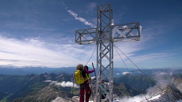 Zwei Bergsteigerinnen unter dem Gipfelkreuz des Weisszint | Bild: BR