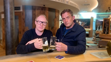 Von links: Simon Schwarz und Sebastian Bezzel trinken ein Bier an der Theke des Bierhotels. | Bild: BR/strandgutmedia GmbH/Benjamin Frank