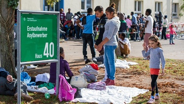 Mehrere Flüchtlinge stehen in München (Bayern) mit ihren Koffern auf dem Gelände der Bayernkaserne vor der Erstaufnahme für Asylbewerber. | Bild: picture-alliance/dpa