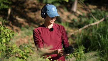 Eine Frau läuft mit Kopfhörern und Richtmikrofon durch den Wald | Bild: BR 
