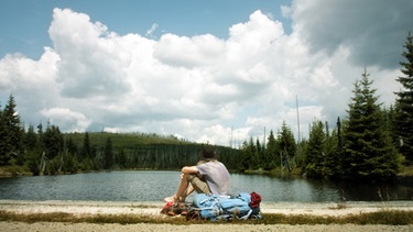 Mann sitzt vor einem See mit Wald im Hintergrund | Bild: Still aus dem Film: Der wilde Wald