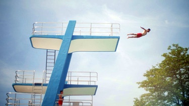 Sprungturm im Schwimmbad (von seitlich unten). Ein Mann springt mit geradem Körper und  seitlich ausgestreckten Armen vom obersten Turm. Die Momentaufnahme zeigt ihn in der Luft vor blauem Himmel. | Bild: BR
