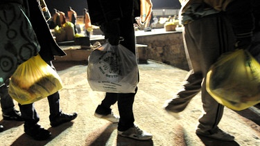 Symbolbild: Die Beine und Schatten von drei jungen Männern auf der Flucht, mit Plastiktüten in der Hand | Bild: picture-alliance/dpa