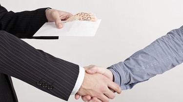 Zwei Männer schütteln sich die Hände, einer hält ein Kuvert mit Geldscheinen in der Hand | Bild: picture-alliance/dpa