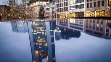 Die Zentrale der Commerzbank steht in Frankfurt am Main (Hessen) im Morgenlicht und spiegelt sich in einem Autodach. | Bild: picture-alliance/dpa