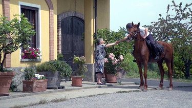 Ein Reiter gibt vom Pferd aus seine Hand einer Frau. | Bild: BR