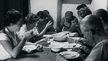 Eine Familie sitzt um einen Tisch beim Essen herum | Bild: BR