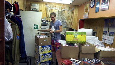 Ein Mann packt in einem engen Raum Kartons. | Bild: BR
