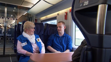 Eine Frau von der Bahnhofsmission begleitet einen Mann im Zug. | Bild: BR