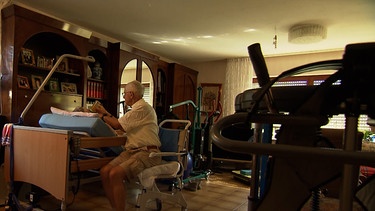 Mann im Wohnzimmer mit Pflegegeräten. | Bild: BR