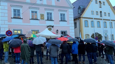 Menschen mit Regenschirmen stehen zusammen-. | Bild: BR