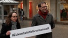 Wirtschaftsreferentin Andrea Heilmaier und Baureferent Daniel Ulrich halten ein Schild der #ZukunftsinitiativeInnenstadt hoch. | Bild: BR