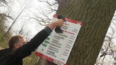 Ein Mitgleid des Fränkischen Albvereins montiert das letzte der 90 Schilder, die zukünftig Wanderer durchs Hammerbachtal leiten sollen. | Bild: BR