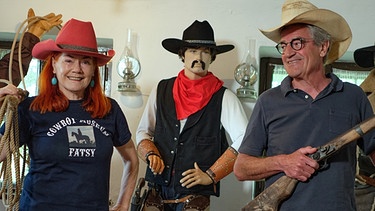 Franz X. Gernstl besucht das Cowboy-Museum in Linz. Zusammen mit Ilse Ratzenböck, die für das Museum über 5.000 Exponate aus dem Wilden Westen zusammengetragen hat, posiert er mit Cowboy-Hut und Flinte. | Bild: BR/megaherz gmbh/HP Fischer