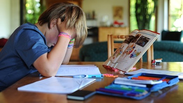 Ein Junge hält sich beim Erledigen seiner Hausaufgaben den Kopf.  | Bild: picture-alliance/dpa