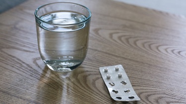 Ein Glas Wasser mit Tabletten in Blisterverpackung. | Bild: BR/Lisa Hinder