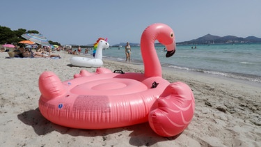 11.07.2021, Spanien, -: Ein aufblasbarer rosa Flamingo liegt am Strand von Playa de Muro im Norden von Mallorca. Die Bundesregierung hat ganz Spanien mit Mallorca und den Kanaren angesichts rapide ansteigender Corona-Zahlen zum Risikogebiet erklärt. Die praktischen Auswirkungen für Mallorca-Urlauber halten sich zunächst aber in Grenzen. Foto: Clara Margais/dpa +++ dpa-Bildfunk +++ | Bild: dpa-Bildfunk/Clara Margais