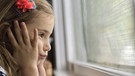 Ein Mädchen schaut traurig aus einem Fenster. | Bild: picture-alliance/dpa