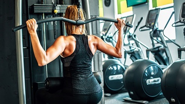 Eine Frau trainiert im Fitnessstudio ihre Rückenmuskulatur. | Bild: stock.adobe.com/insomniafoto