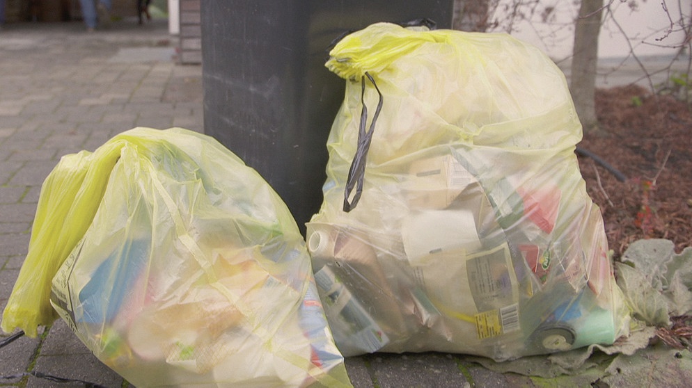 Zwei gelbe Säcke stehen neben einer Mülltonne. Viele Kunststoffe lassen sich nicht sortenrein sortieren. Verpackungen mit fluoreszierenden Markern könnten diesen Job übernehmen.  | Bild: BR/Gut zu wissen