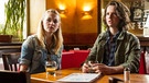 Jens Tochter Peggy (Melina Borcherding, rechts) sitzt mit ihrer Freundin Micha (Teresa Klamert) im Cafe und entdeckt ihren Vater an der Bar.  | Bild: BR/Chris Hirschhäuser