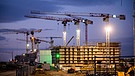Baukräne stehen am frühen Morgen in einem Neubaugebiet. | Bild: picture alliance/dpa | Julian Stratenschulte